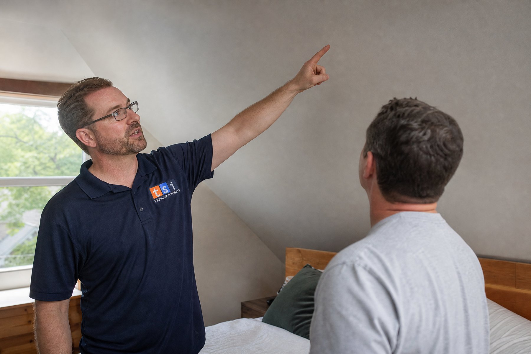 TSI installer in branded uniform discussing new skylight placement with a homeowner in their attic room